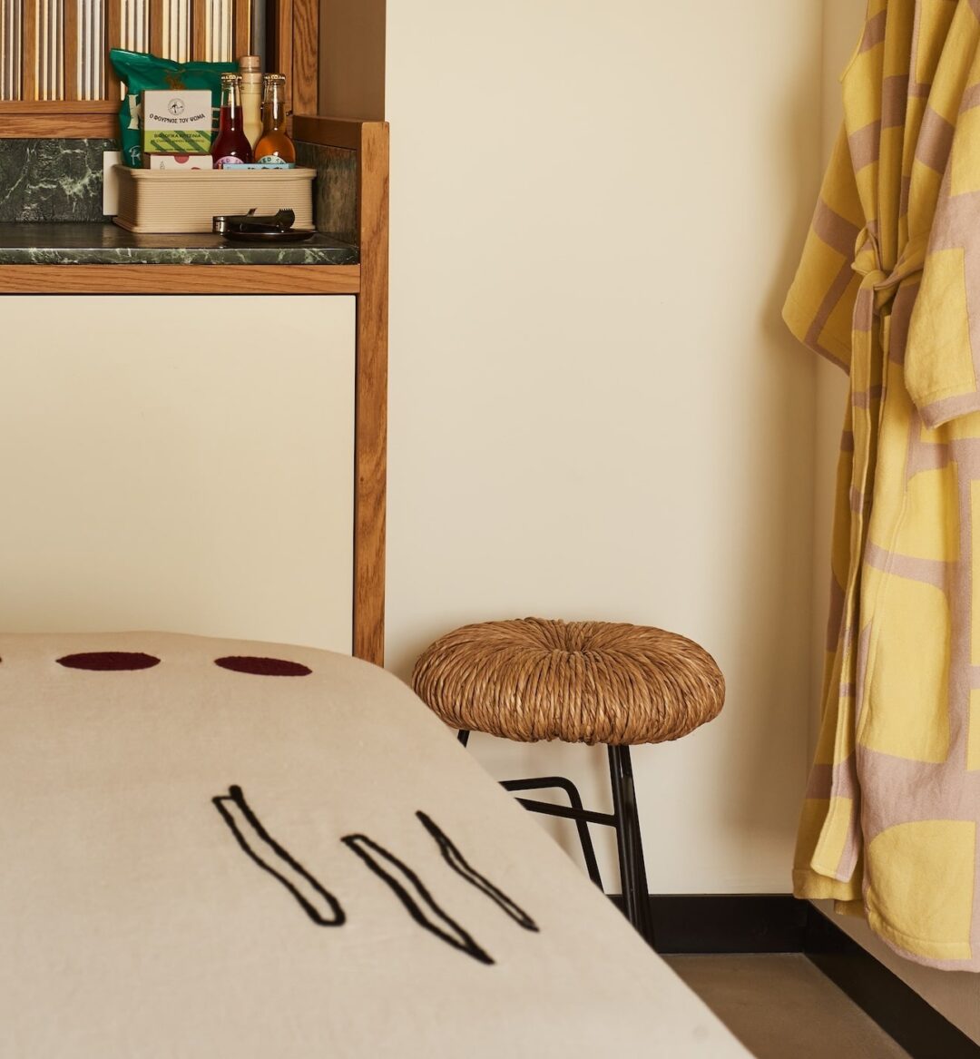 Cozy room corner with a yellow robe on a wall hook, woven stool, and a wooden countertop holding snacks and drinks. Warm, inviting atmosphere.