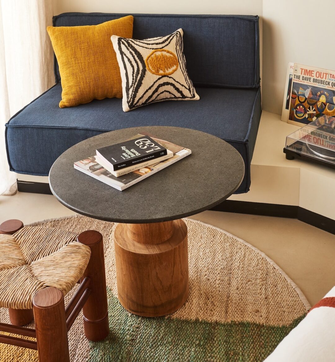 A room featuring a couch, small table, stool, colorful pillow, and a record player.