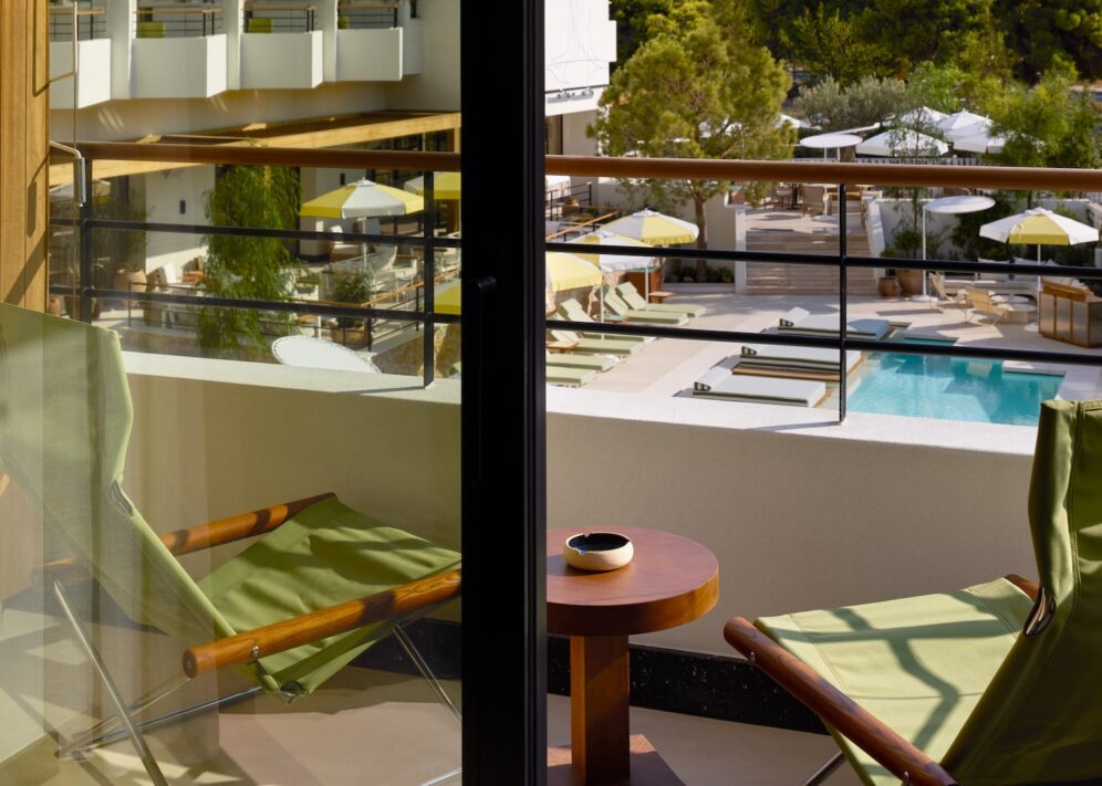 A scenic view of a sparkling pool seen from a cozy balcony, surrounded by lush greenery.