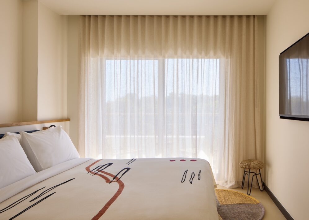 Bright bedroom with a spacious bed, a TV, and tall windows that enhance the airy atmosphere.