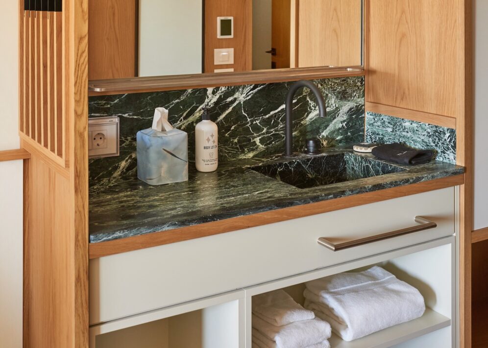 Stylish bathroom showcasing a marble countertop, wooden cabinets, and tall windows that bring in plenty of sunlight.