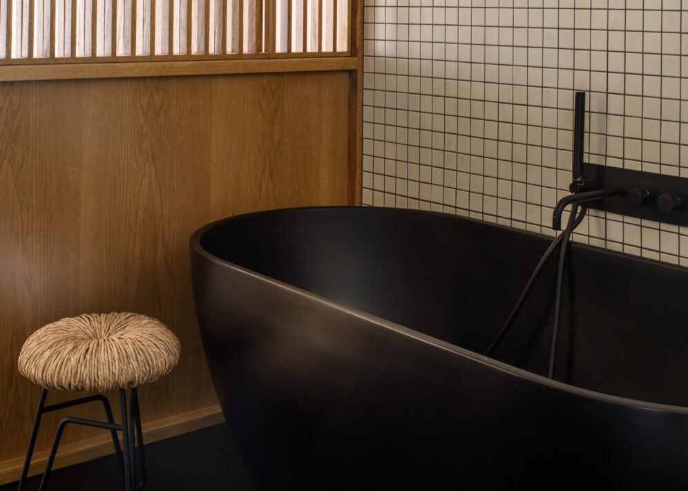 A sleek black bathtub in a stylish bathroom, accompanied by a wooden stool nearby.
