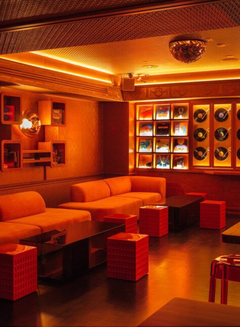 Libera corner sofa dining area with orange lit lights, vinyl record background wall and small tables.