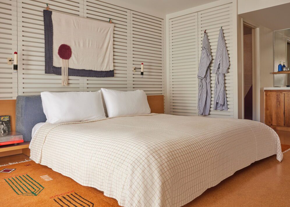 A bed with plaid bedding is drenched in natural light and an ornate brown rug adorns the floor