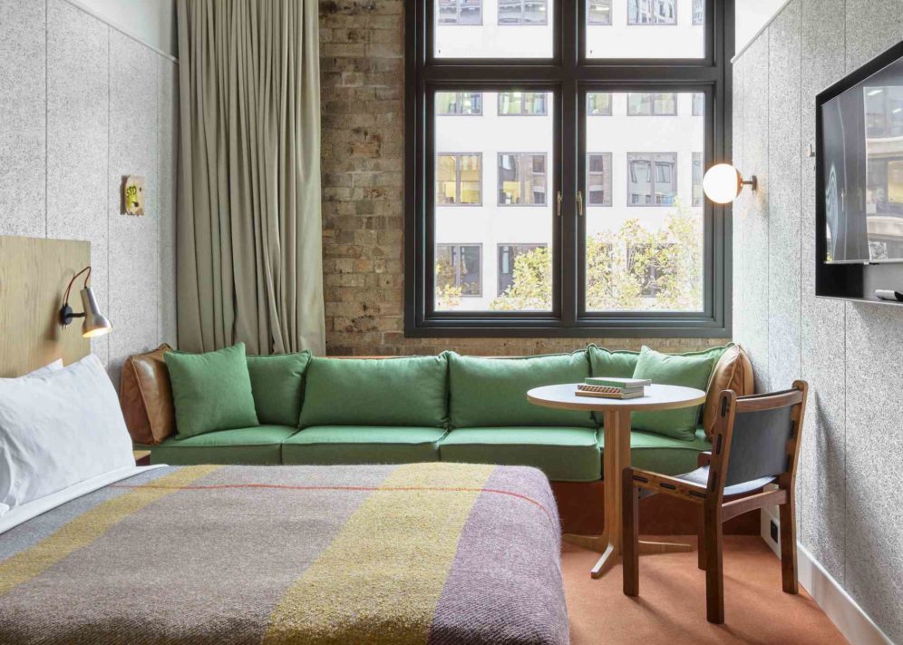 A long, green sofa sits against an exposed brick wall. A table and chair is next to the sofa, providing ample seating space